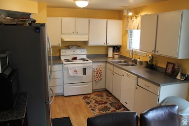 Kitchen featuring white appliances, under cabinet range hood, white cabinetry.