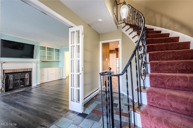 Staircase with baseboard heating, a brick fireplace, french doors, and wood finished floors