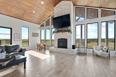 Living room with light hardwood / wood-style flooring, a wealth of natural light, a stone fireplace, and wood ceiling