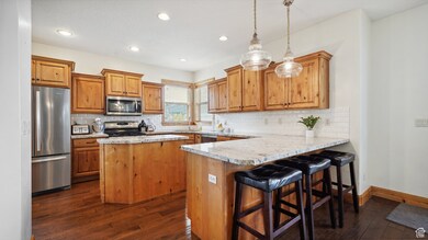 Kitchen with stainless steel appliances, a peninsula, a sink, brown cabinetry, and dark wood-type flooring