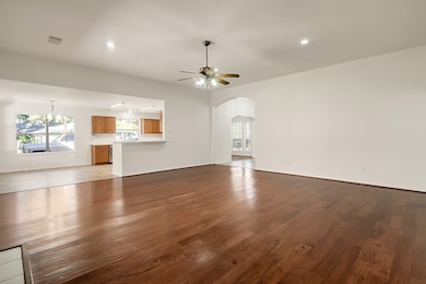Spacious open-concept living area with rich hardwood floors, a ceiling fan, and plenty of natural light. The kitchen features wooden cabinets and a large window. An archway leads to additional rooms, enhancing the home's flow.