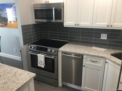 Kitchen with white cabinets, appliances with stainless steel finishes, light stone counters, dark tile patterned flooring, and backsplash