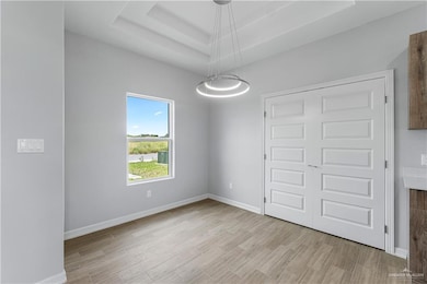 Unfurnished bedroom featuring a raised ceiling, light wood finished floors, and baseboards