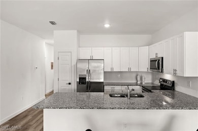 Kitchen with white cabinetry, sink, appliances with stainless steel finishes, dark stone countertops, and dark hardwood / wood-style floors