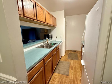 Kitchen featuring brown cabinetry, light wood-style floors, white appliances, and light countertops