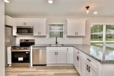 Images are of a model home and may include custom design features not available in other homes. Kitchen with stainless steel appliances, white cabinetry, recessed lighting, light stone countertops, and a peninsula