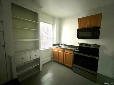 Kitchen with electric range, brown cabinets, black microwave, and dark countertops