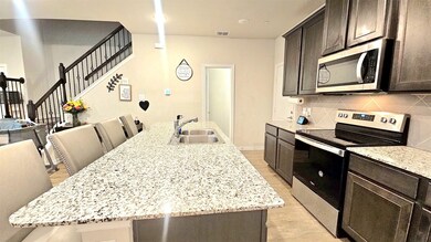 Kitchen with stainless steel appliances, a center island with sink, a breakfast bar, dark brown cabinets, and light stone counters
