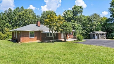 Ranch-style house featuring brick siding, a chimney, a front lawn, and an outbuilding
