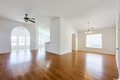 Unfurnished living room with light wood-style floors, arched walkways, a chandelier, ceiling fan, and lofted ceiling