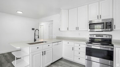 Kitchen with appliances with stainless steel finishes, a peninsula, light wood-style flooring, and white cabinetry