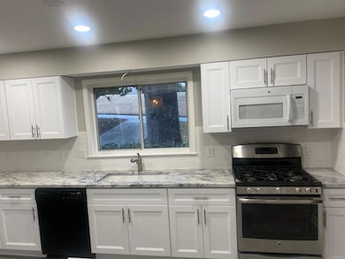 Kitchen featuring white microwave, black dishwasher, stainless steel range with gas cooktop, a sink, and white cabinetry