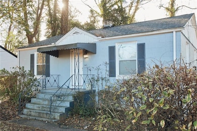 Bungalow with concrete block siding, roof with shingles, and a chimney