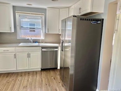 Kitchen with appliances with stainless steel finishes, white cabinets, light wood finished floors, and light countertops