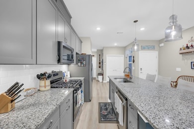Kitchen with stainless steel appliances, light stone counters, light wood-style flooring, decorative light fixtures, and gray cabinetry