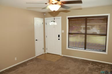 Entrance foyer with ceiling fan, dark colored carpet, and dark tile patterned flooring