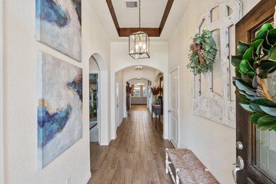 The entryway is framed with stained beams lining the tray ceiling, lantern-style lighting, wood look tile flooring, arched doorways, and plenty of charm.