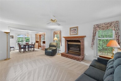 Living room with a fireplace, light colored carpet, ornamental molding, and ceiling fan