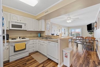 Kitchen featuring ornamental molding, white appliances, white cabinets, a peninsula, and dark wood-type flooring