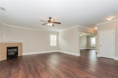 Unfurnished living room featuring a ceiling fan, arched walkways, dark wood-style flooring, crown molding, and a fireplace