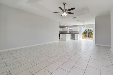Unfurnished living room featuring a raised ceiling, a chandelier, a ceiling fan, and light marble finish floors