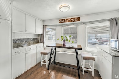 Kitchen with backsplash, light stone countertops, a textured ceiling, white cabinetry, and dark wood-style flooring
