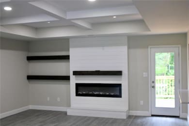 Unfurnished living room with wood finished floors, recessed lighting, beamed ceiling, baseboards, and a glass covered fireplace