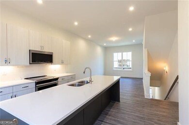 Kitchen with light countertops, appliances with stainless steel finishes, a sink, dark wood-style floors, and a large island with sink