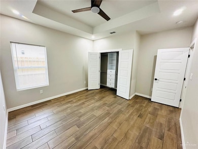 Unfurnished bedroom featuring wood finished floors, a raised ceiling, a closet, and baseboards