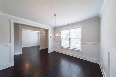 Unfurnished dining area with a chandelier, dark wood-type flooring, a wainscoted wall, crown molding, and a decorative wall
