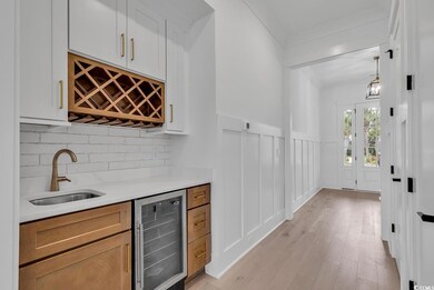 Bar featuring sink, white cabinetry, light wood-ty