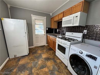 Kitchen featuring washer / dryer, white appliances, backsplash, stone finish flooring, and ornamental molding