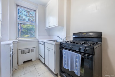 Kitchen with white cabinetry, black gas range, radiator, light countertops, and light tile patterned floors
