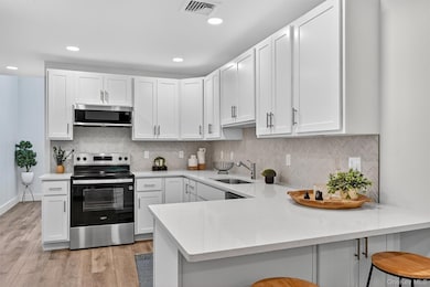 Kitchen with stainless steel appliances, white cabinets, backsplash, a breakfast bar, and recessed lighting