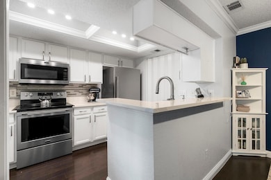 Kitchen with appliances with stainless steel finishes, ornamental molding, white cabinets, backsplash, and dark wood-style flooring