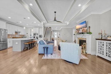 Living room featuring stairs, a brick fireplace, light wood-type flooring, a raised ceiling, and ornamental molding