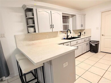 Kitchen featuring light tile patterned floors, a kitchen bar, a peninsula, open shelves, and white cabinets