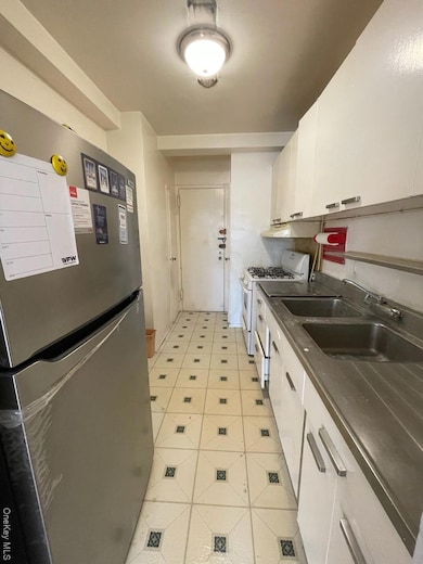 Kitchen featuring a sink, fridge, range, dark countertops, and white cabinets