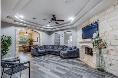 Living room with a chandelier, wood finished floors, a ceiling fan, and a tray ceiling
