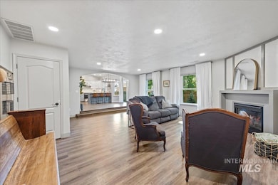 Living room with a glass covered fireplace, light wood-type flooring, recessed lighting, arched walkways, and a chandelier