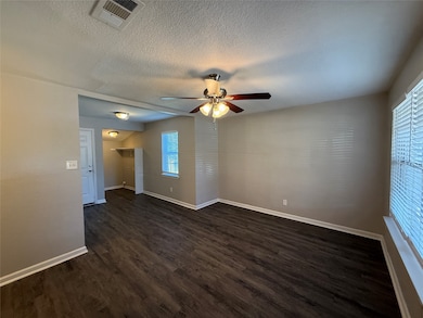 Empty room with dark wood-style flooring, a ceiling fan, healthy amount of natural light, and a textured ceiling