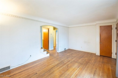 Living room room with arched walkways, hardwood flooring, and wallpapered walls