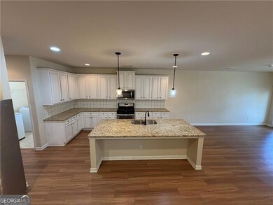 Kitchen with appliances with stainless steel finishes, a sink, an island with sink, baseboards, and dark wood-style floors