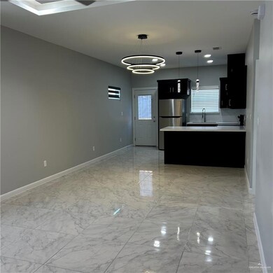 Kitchen with light countertops, light marble finish flooring, dark cabinetry, hanging light fixtures, and a peninsula