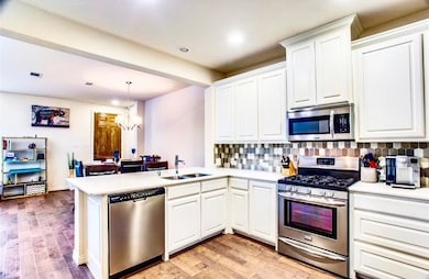 Kitchen featuring stainless steel appliances, pendant lighting, white cabinets, decorative backsplash, and a chandelier