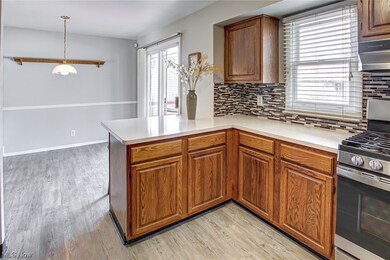 Kitchen with light wood-type flooring, range hood, gas stove, tasteful backsplash, and kitchen peninsula