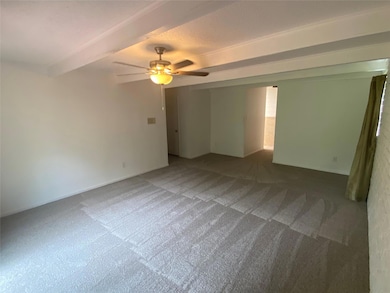 Carpeted empty room with ceiling fan and beam ceiling
