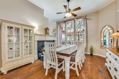 Dining area with ornamental molding, dark wood finished floors, a tiled fireplace, and a ceiling fan