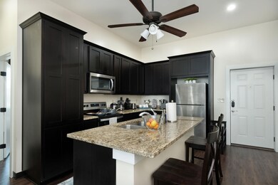 Kitchen with dark cabinetry, dark wood-style flooring, appliances with stainless steel finishes, and light stone counters