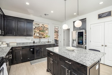 Kitchen featuring light stone countertops, light wood-type flooring, decorative light fixtures, black dishwasher, and recessed lighting